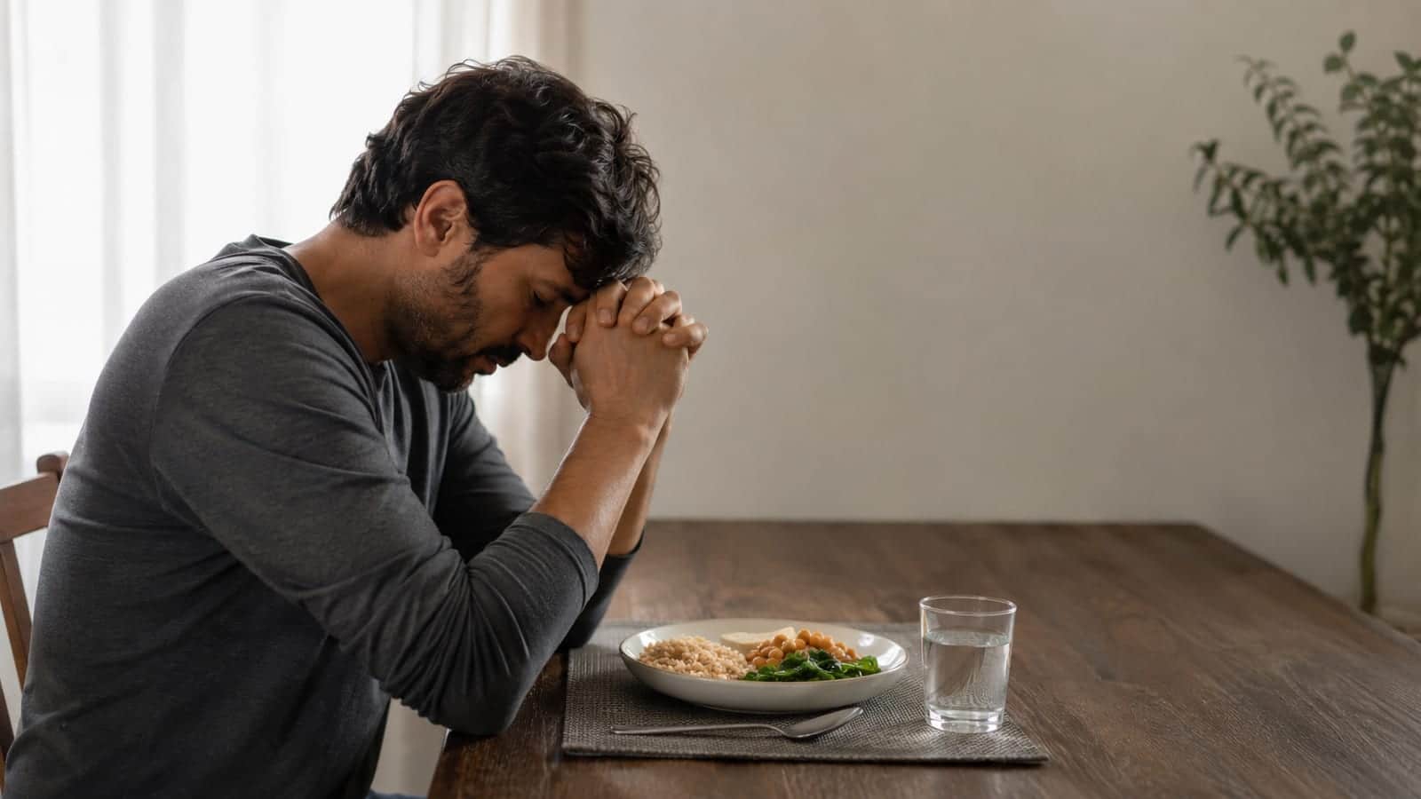 A weary adult praying beside an untouched simple meal during a quiet home fast